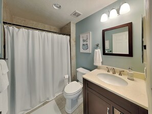 A bathroom with a shower curtain, toilet, sink, and mirror. - Surf Club by VTrips (Palm Coast)