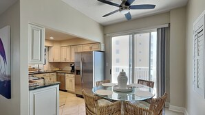 A modern kitchen with white cabinets, a stainless steel refrigerator, and a glass dining table surrounded by wicker chairs. - Surf Club by VTrips (Palm Coast)