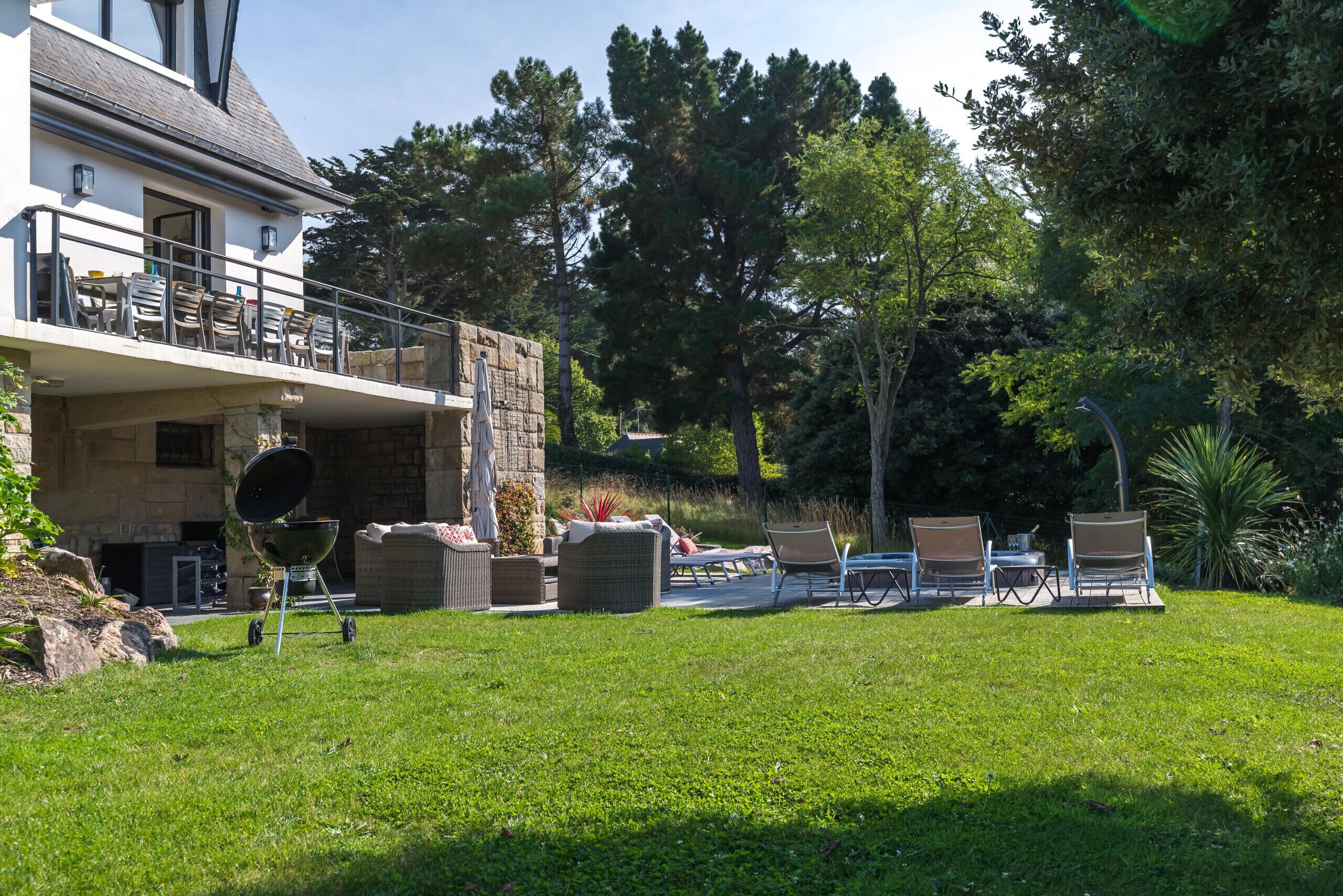 Une maison à deux étages dotée d’un balcon, d’un espace extérieur aménagé pour s’asseoir et d’un mur en pierre.