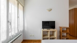 A bedroom with a bed, a TV on a wooden stand, a wardrobe, and a window with curtains. - Urban Cozy Apartment by Wonderful Italy (Bologna)