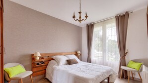 A bedroom with a large bed, wooden headboard, bedside tables with lamps, a chair with a cushion, and a window with curtains. - House for 5 - 300m from Tanchet beach (Les Sables-d´Olonne)