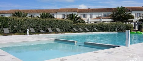 A swimming pool with lounge chairs and a building with a tiled roof in the background.