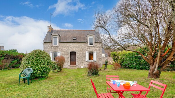 Une maison en pierre avec une cour verdoyante, une table à manger avec des chaises rouges et un grand arbre.