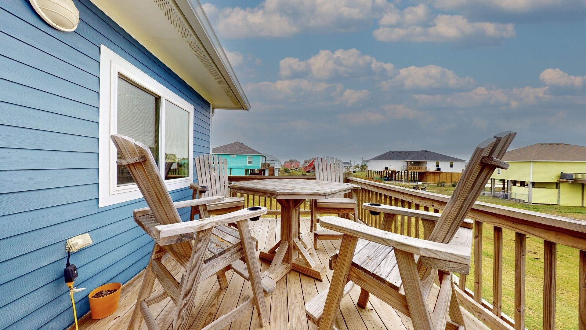 A wooden deck with a table and chairs, a potted plant, and a view of neighboring houses.