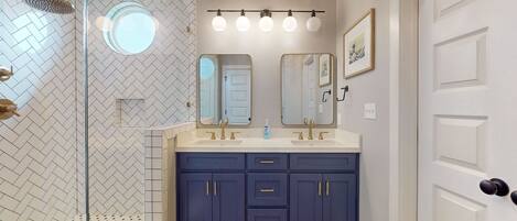 Une salle de bain avec une douche, deux lavabos et un grand miroir.