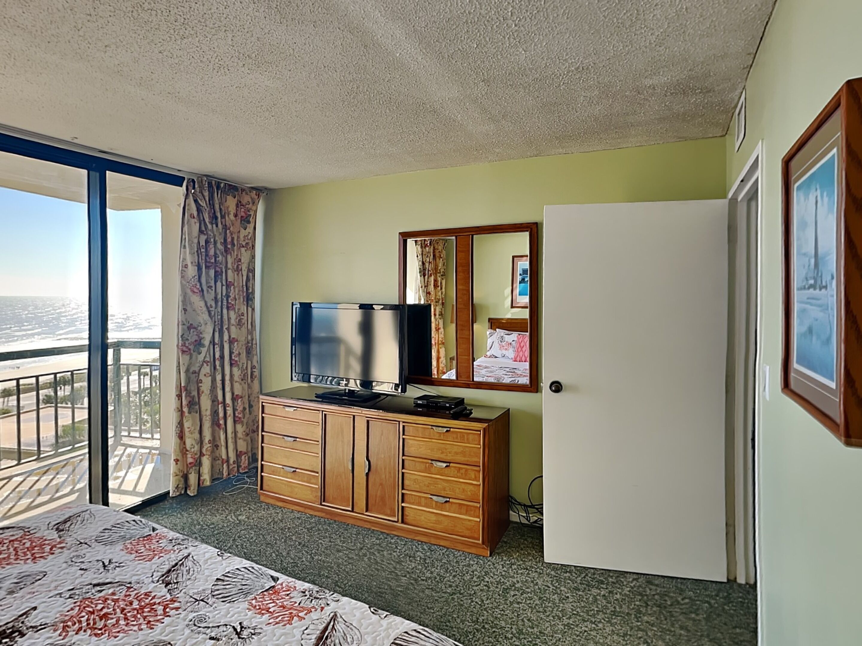 Une chambre d’hôtel avec un grand lit, une commode en bois, une télévision, un miroir et une porte.