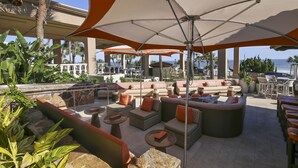 A sunlit outdoor lounge area with multiple seating options, including sofas and chairs, under large umbrellas. - San Luis Manor by Ryson Vacation Rentals (Galveston)
