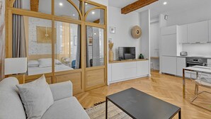 Una sala de estar moderna con un sofá, una mesa de centro y un televisor. Cuenta con una zona de cocina con armarios y una mesa de comedor.