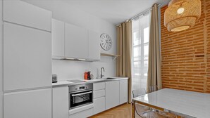 Cocina moderna con armarios blancos, horno integrado, lavamanos y una mesa de comedor con sillas.