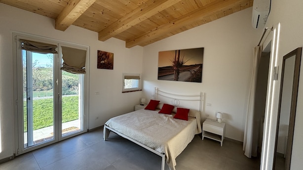 A bedroom with a bed, a window, a painting, and a door. - Brand New Farmhouse in Splendid Location for Exploring the Northern Marche Region (Castelvecchio)