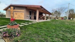 A building with a 'Welcome' sign, a covered porch, and a garden with flowers. - Brand New Farmhouse in Splendid Location for Exploring the Northern Marche Region (Castelvecchio)