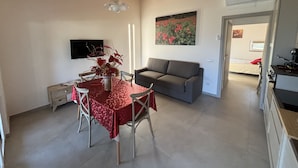 A dining area with a table and chairs, a gray sofa, and a painting on the wall. - Brand New Farmhouse in Splendid Location for Exploring the Northern Marche Region (Castelvecchio)