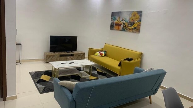 A modern living room with a blue sofa, a yellow sofa, a flat-screen TV, and a painting on the wall. - L'Oasis Mid-Century (Cotonou)