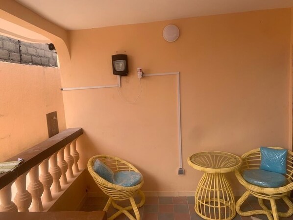 A balcony with a railing, two wicker chairs with cushions, a small round table, and a wall-mounted electrical outlet.