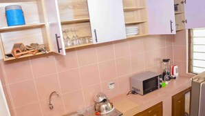 A kitchen with a sink, a kettle, a microwave, and various utensils on shelves. - L'Oasis Mid-Century (Cotonou)
