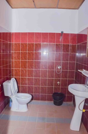 A bathroom with red tiled walls, a white toilet, a black bucket, and a white sink.