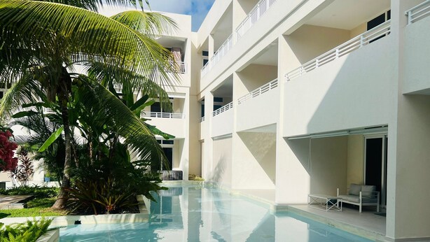 Ein Poolbereich mit freier Sicht auf den Pool, umliegendes Grün und ein mehrstöckiges Gebäude mit Balkonen.