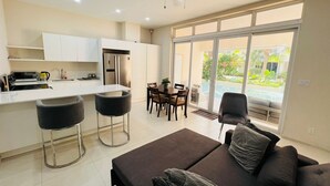 Eine moderne Küche mit weißen Schränken, einem eingebauten Backofen und einem Kühlschrank. Es gibt einen Essbereich mit Tisch und Stühlen sowie eine große Schiebeglasdoor zum Pool.