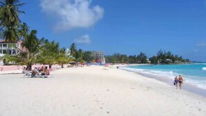 Ein Strand mit Palmen, blauem Himmel und einigen Spaziergängern.