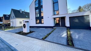 A modern two-story house with a large garage, a paved driveway, and a small garden area. - NEU Luxuswohnung in Waldrandlage Nähe Köln Messe! (Leverkusen)