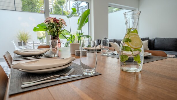 A dining table set with plates, cutlery, and a pitcher of water with mint leaves. - NEU Luxuswohnung in Waldrandlage Nähe Köln Messe! (Leverkusen)