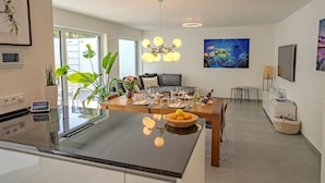A modern kitchen with a central island, dining area with a table set for four, and a living space with a sofa and artwork. - NEU Luxuswohnung in Waldrandlage Nähe Köln Messe! (Leverkusen)