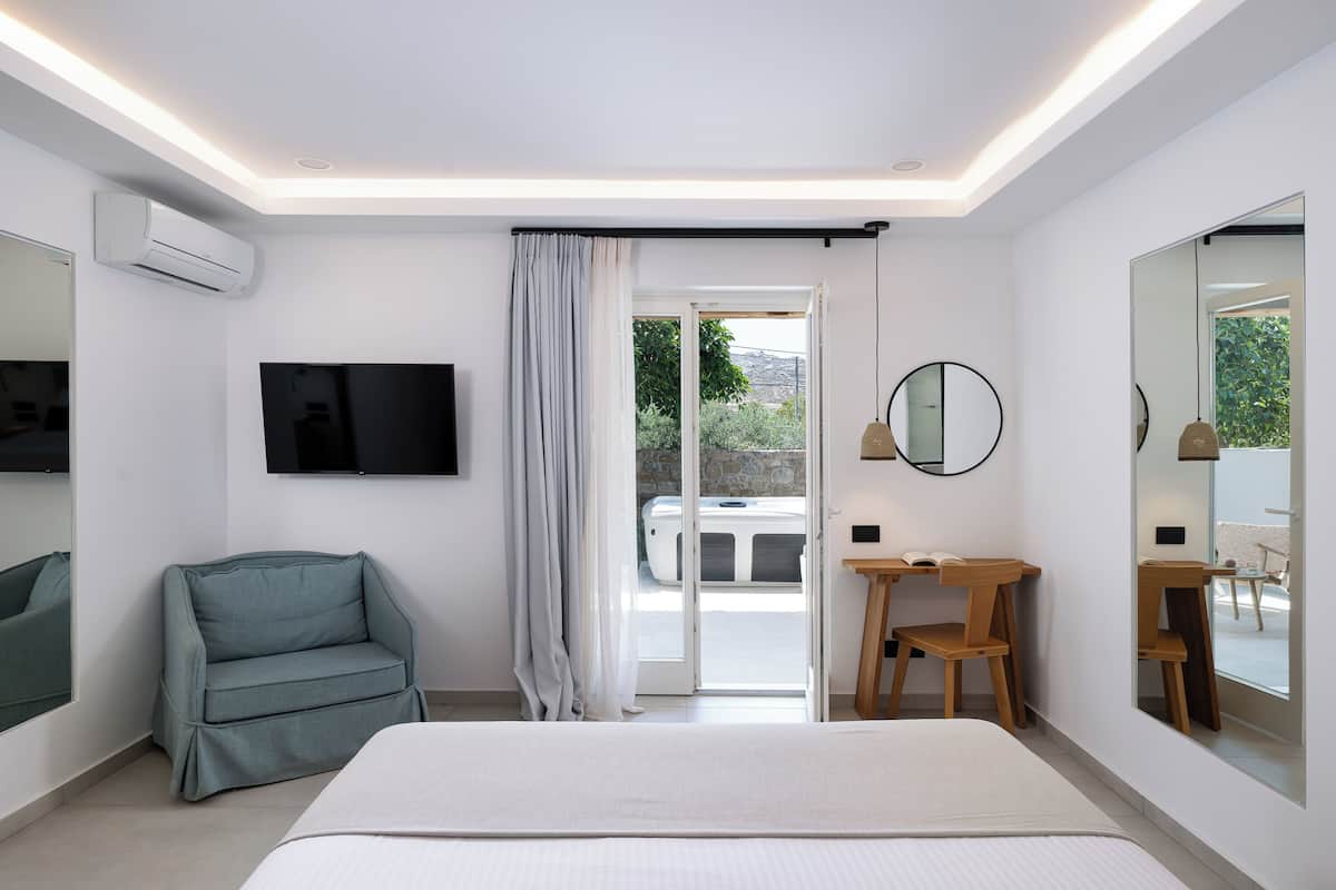 Ein modernes Schlafzimmer mit Bett, Fernseher, Sessel, Schreibtisch und großem Spiegel.