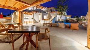 Un espacio de comedor al aire libre con mesas y sillas de madera, una escalera y una piscina.