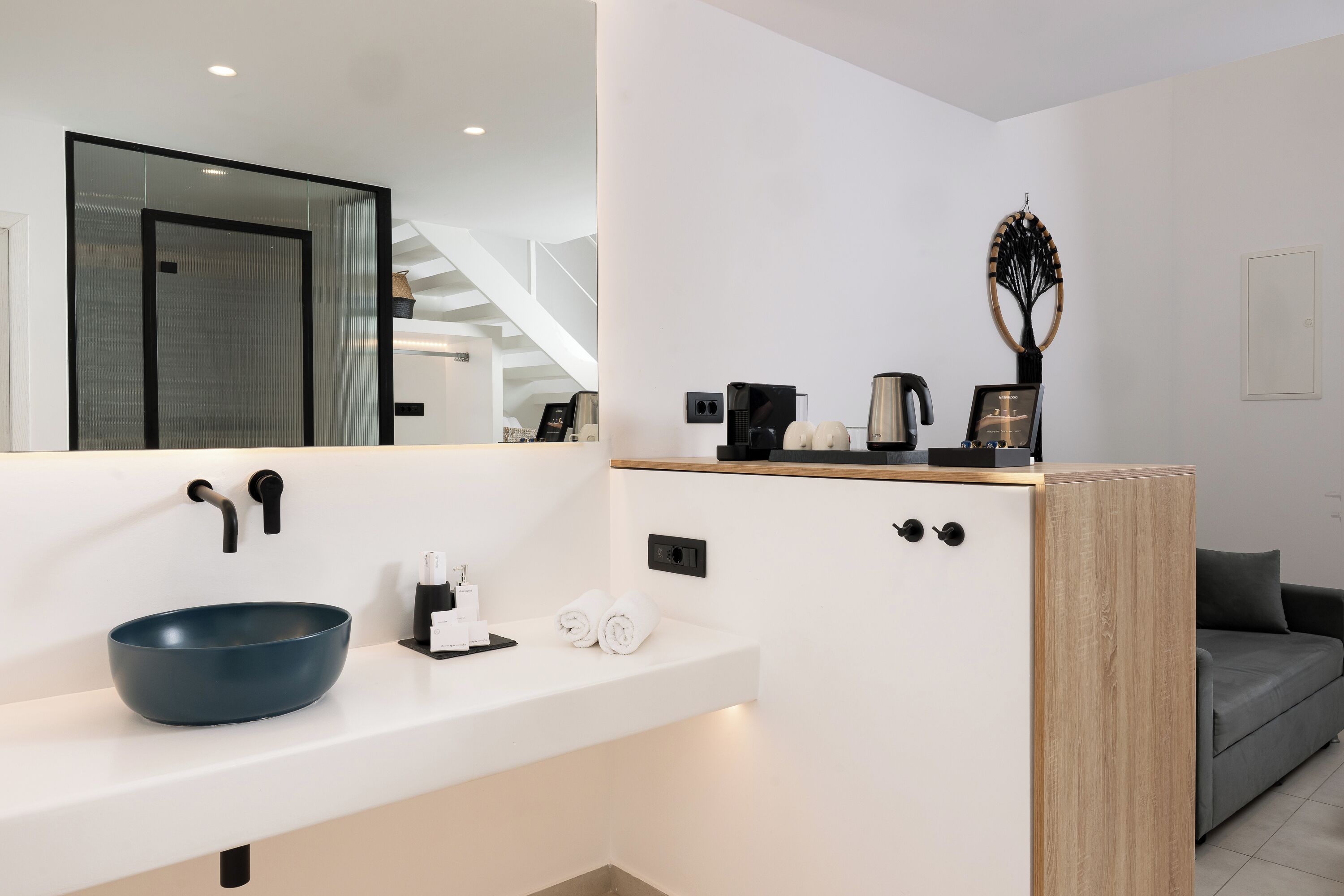 A modern bathroom with a large mirror, a blue basin, a coffee machine, and a decorative tree sculpture.