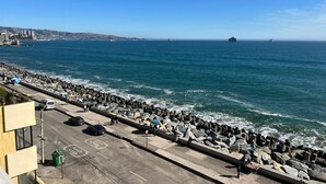 A coastal road with a rocky breakwater, a clear blue sky, and a distant ship.