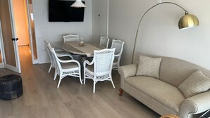 A dining area with a round table, white wicker chairs, and a beige sofa.