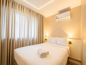 A hotel room with a neatly made bed, an air conditioning unit mounted on the wall, and a window with curtains. - 1 room apartment versatile (Curitiba)