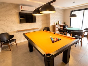 A pool table with a billiard cue and balls, a clock, and a small plant on a shelf.