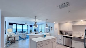 A modern kitchen with white cabinetry, a central island, and a dining area with a view of the ocean.