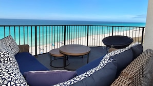 A balcony with a view of the ocean, a wicker sofa, two small round tables, and a black chair.