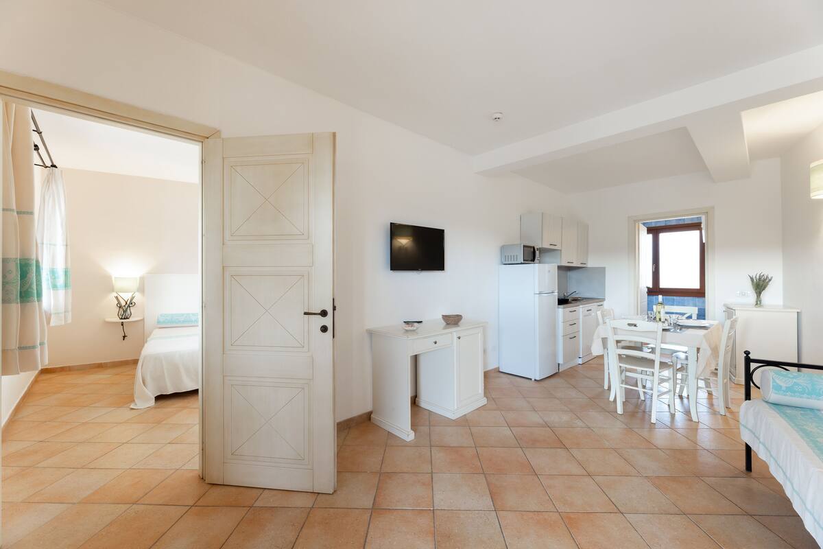 Una habitación pequeña con cama, escritorio, mesa y kitchenette.