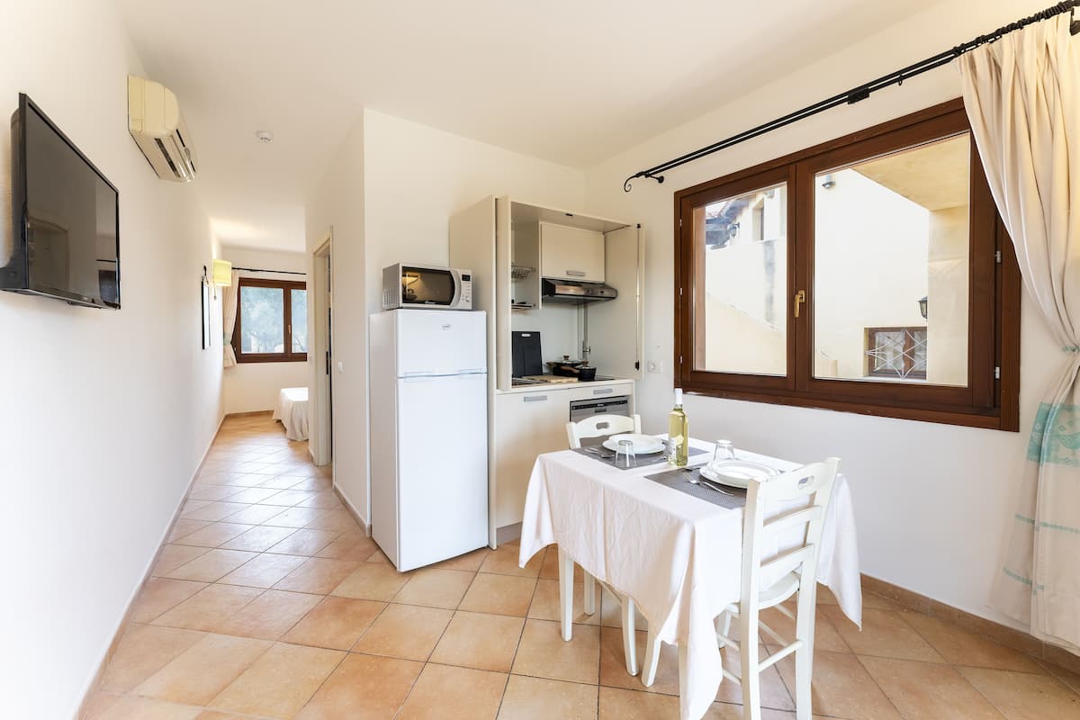 Una cocina compacta con refrigerador, microondas y estufa, una mesa de comedor con sillas y una ventana con cortinas.