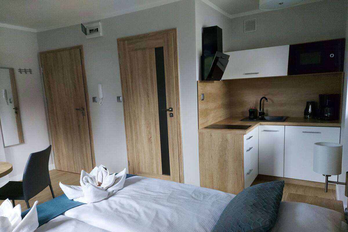 Une chambre d’hôtel comprenant un lit, une petite kitchenette, une armoire en bois et un bureau avec une chaise.