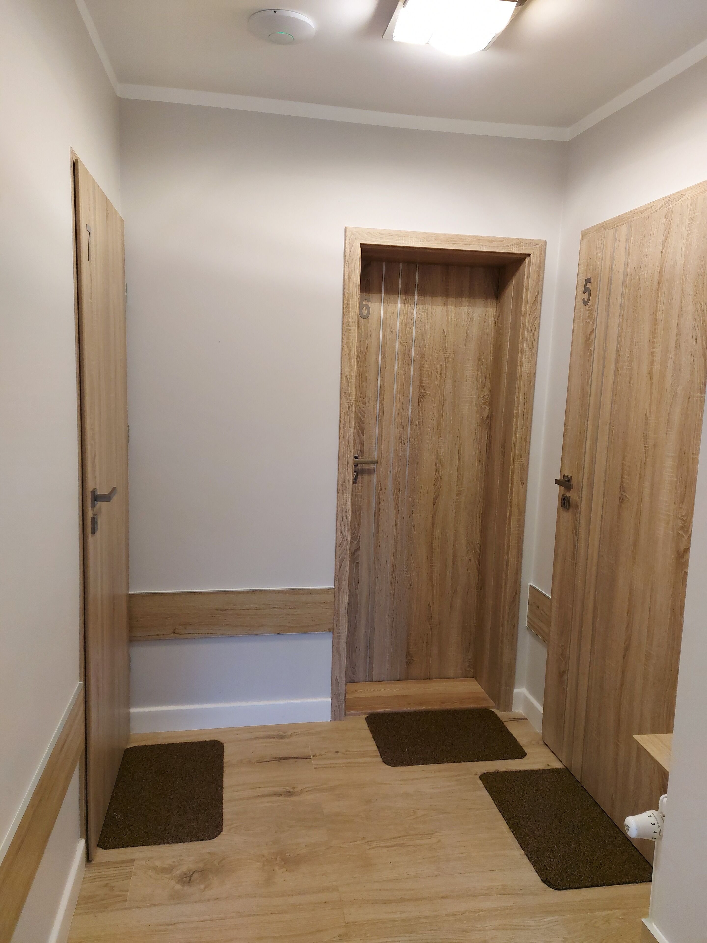 Um corredor com portas de madeira numeradas 5 e 6, teto branco e luminária.