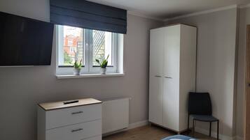 Un dormitorio con cama, armario, escritorio con silla, radiador y ventana con plantas.