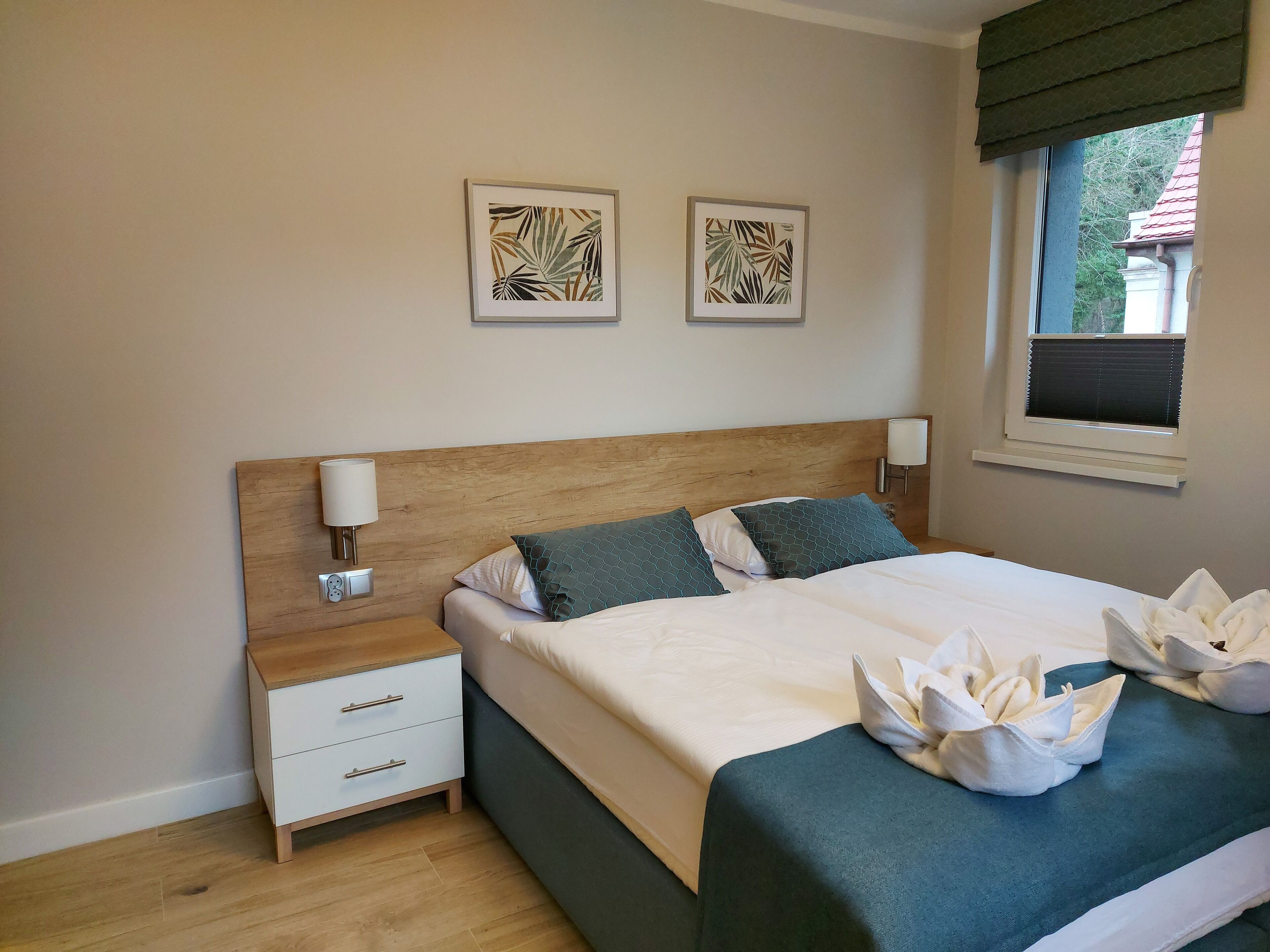 Un lit bien fait, avec une tête de lit en bois, deux tables de chevet avec des lampes et des œuvres d’art accrochées au mur.