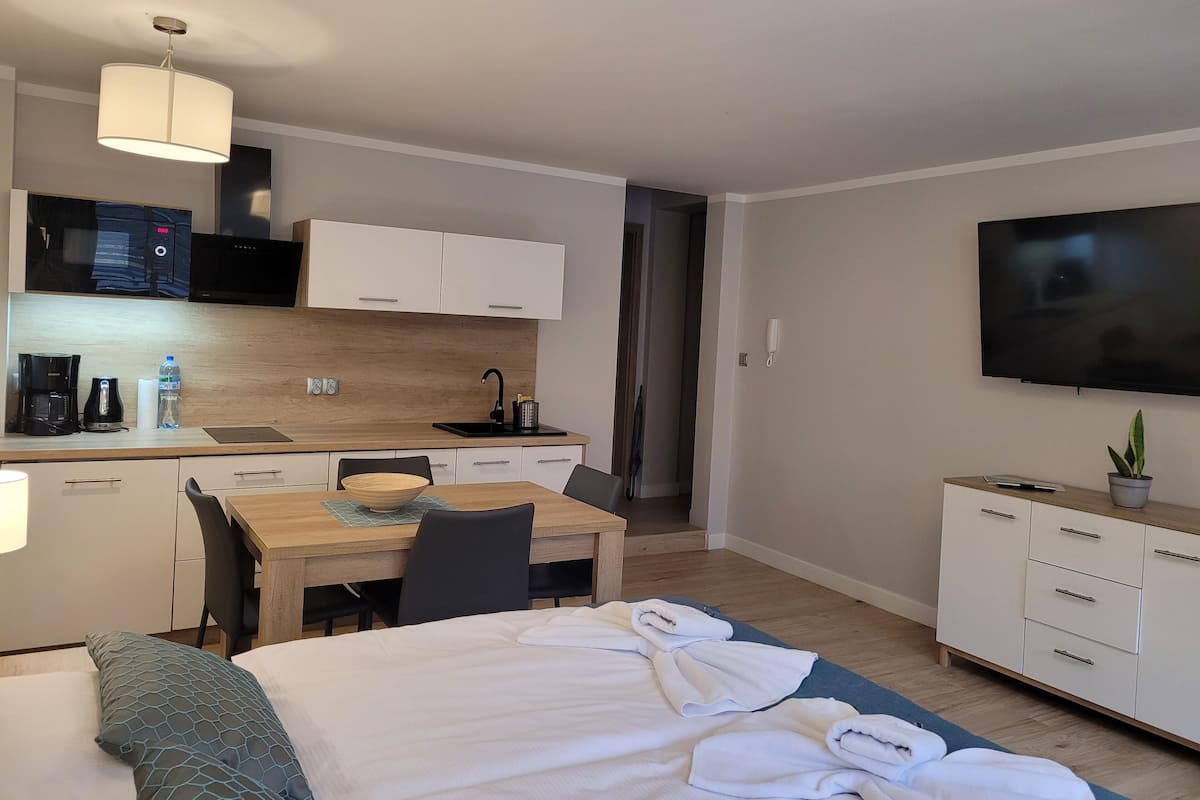 Une chambre d’hôtel moderne équipée d’un lit, d’un bureau avec une chaise, d’une kitchenette et d’un téléviseur.