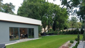 Een modern huis met een grote glazen deur, een verzorgd gazon en een terras met tuinmeubilair.
