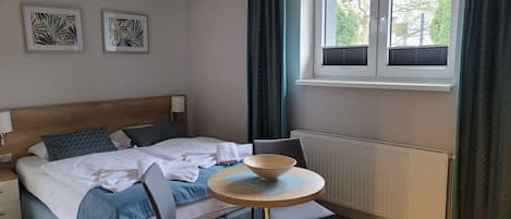Un dormitorio ordenado con cama, mesita de noche y una pequeña mesa redonda con un cuenco.