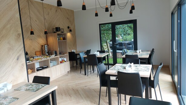 Een moderne eetruimte met houten wanden, zwarte stoelen en tafels. Er hangen hangende lampen en een groot raam met uitzicht op groen.