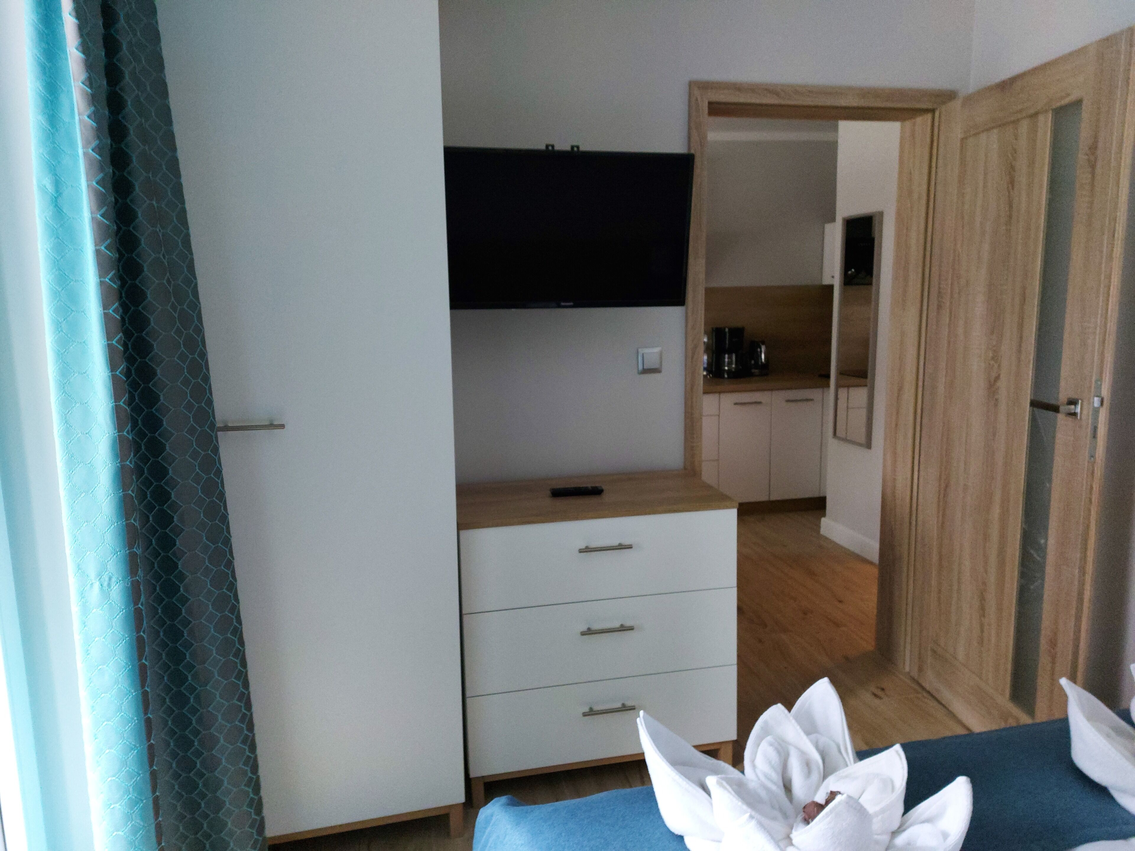 A compact hotel room with a bed, a small desk, a wardrobe, and a kitchenette.