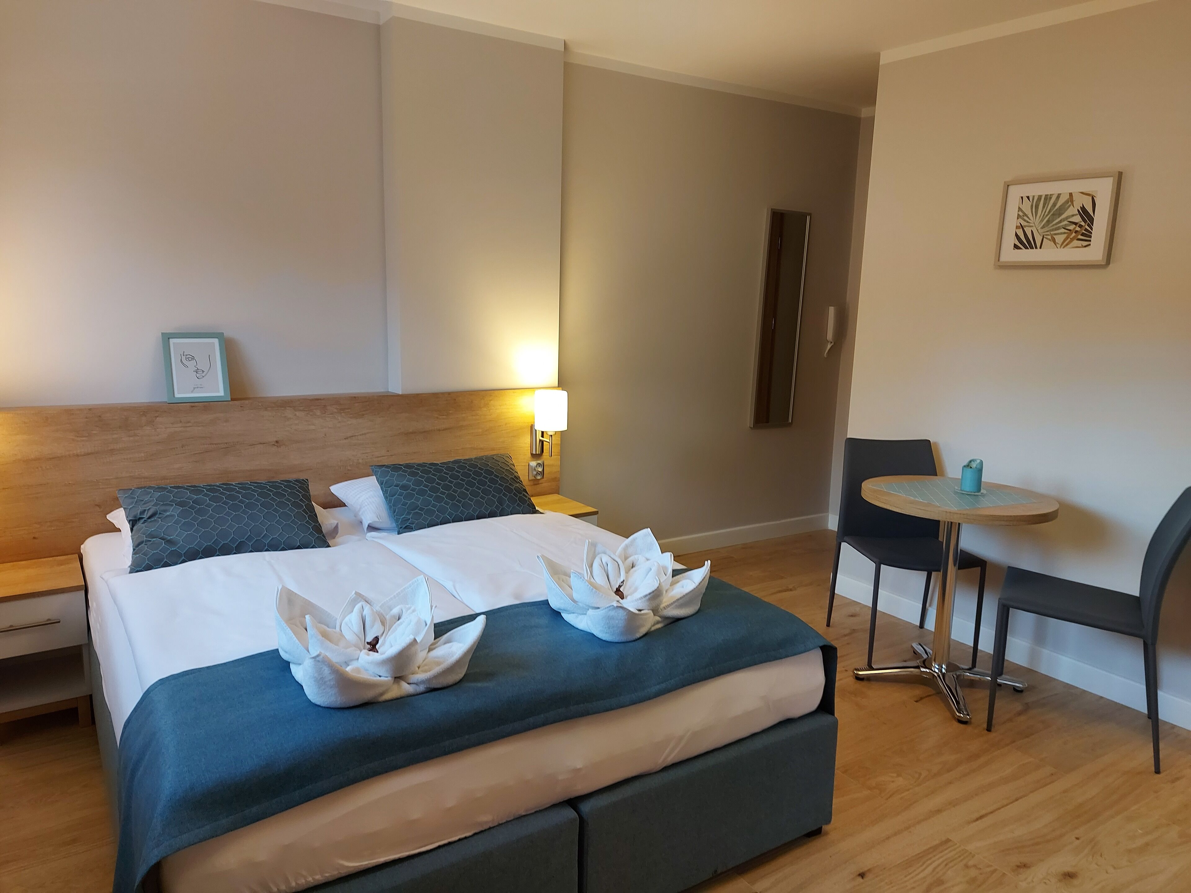 Een hotelkamer met een bed, nachtkastje, lamp, stoel en een kleintje tafeltje met een kop.