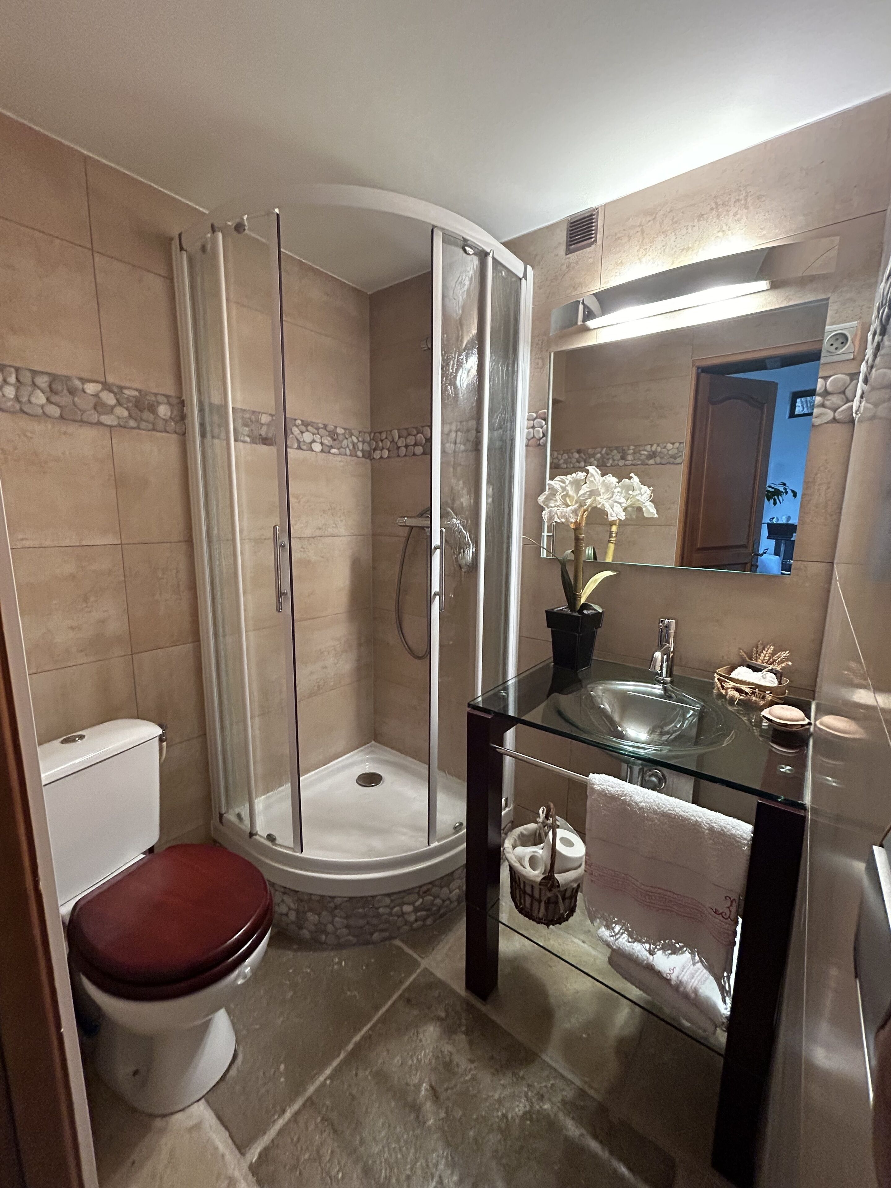 A bathroom with a glass shower enclosure, a toilet, and a glass sink with a mirror above it.