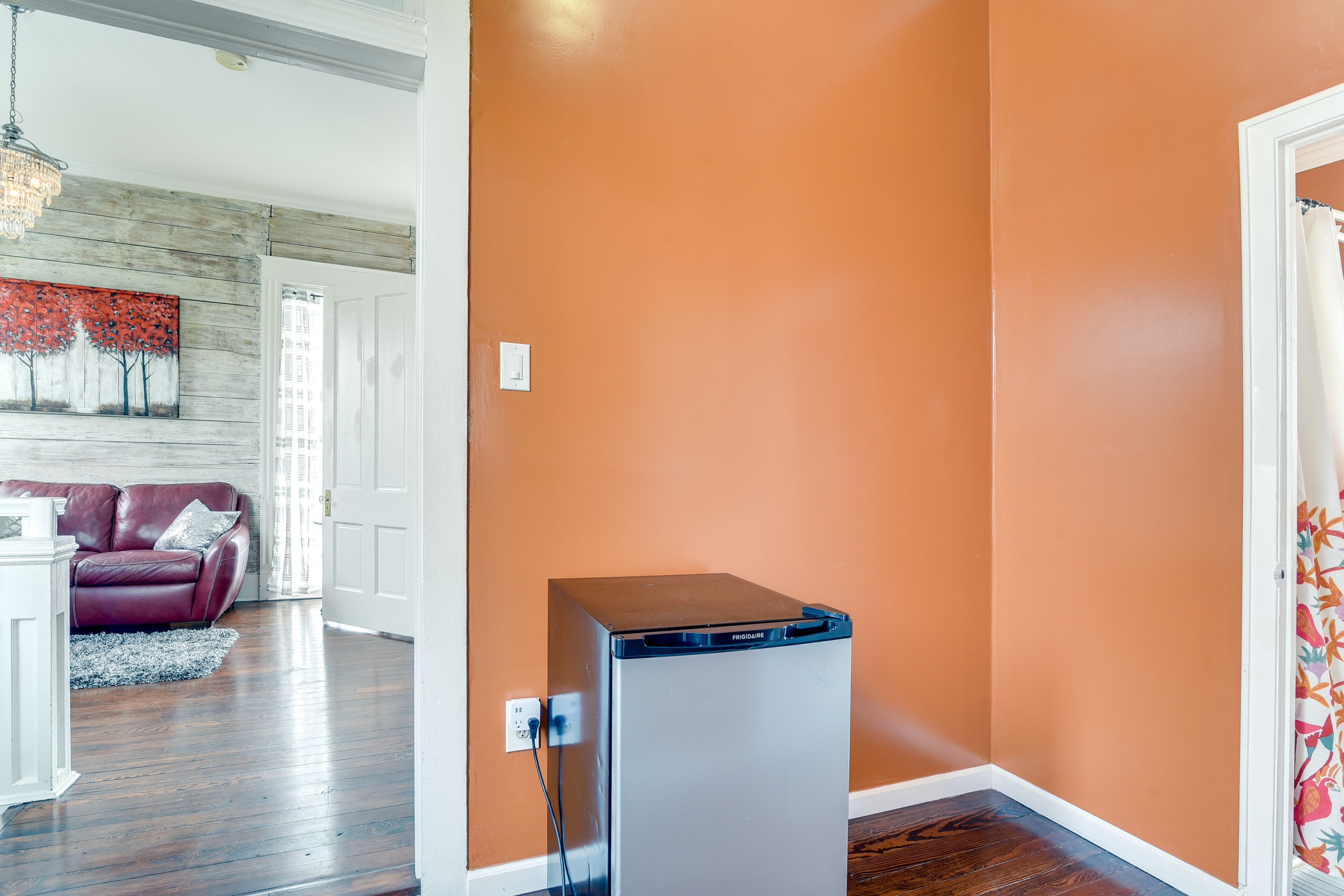 A compact living space with a refrigerator, a wooden floor, a red leather sofa, and a white door.