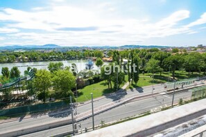Un parque junto al río con un parque infantil, un puente y una calle con tranvía.